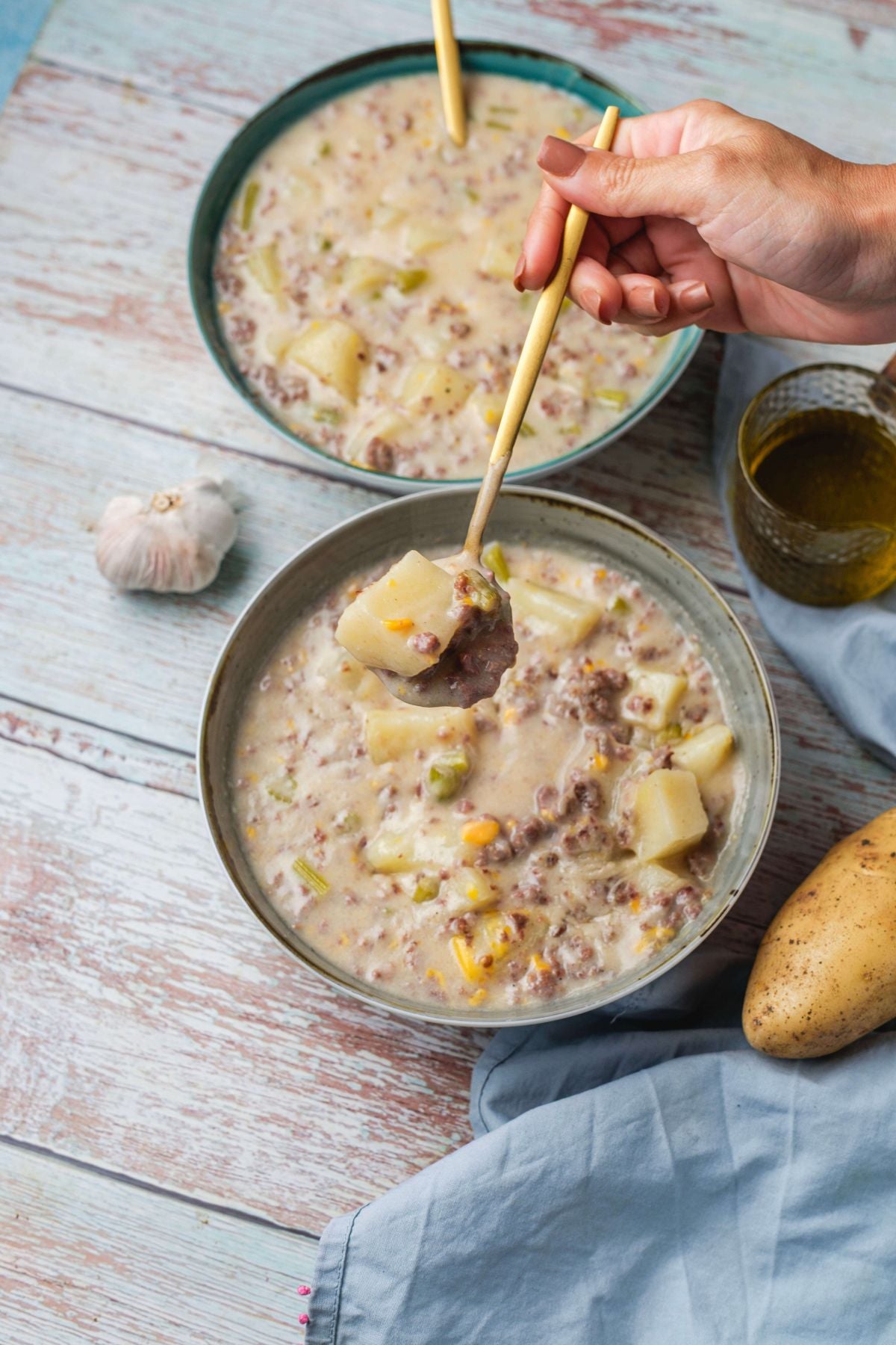 Person eating creamy potato and sausage soup from a bowl with a wooden spoon.